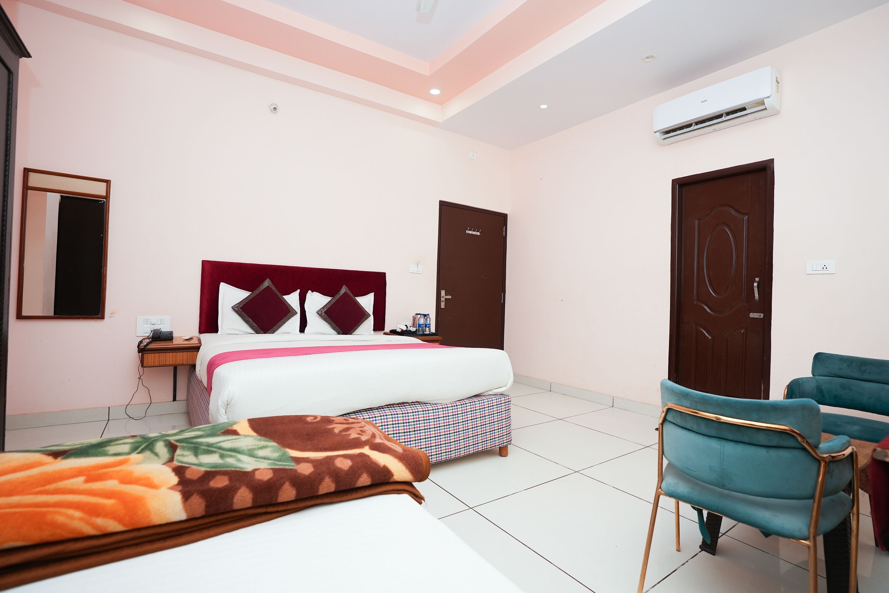 A hotel room with a bed, bedside table, chair, and an air conditioning unit.