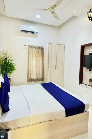 Une chambre à coucher comprenant un lit, un ventilateur de plafond, un climatiseur, une armoire, un téléviseur et une plante en pot.