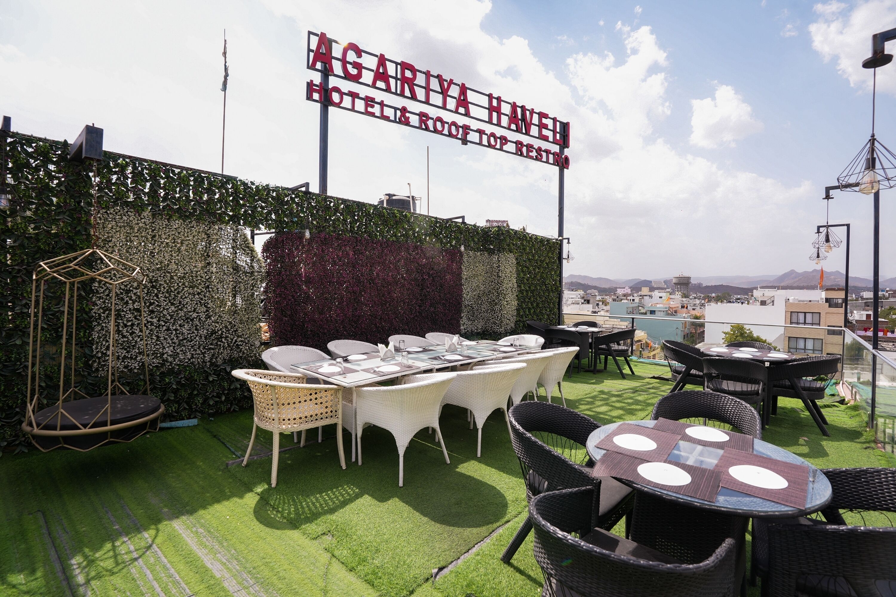 Un espace extérieur aménagé avec des tables et des chaises, une enseigne indiquant l’hôtel Agariya Haven et ses toilettes situées sur le toit, et une vue sur le paysage urbain en arrière-plan.