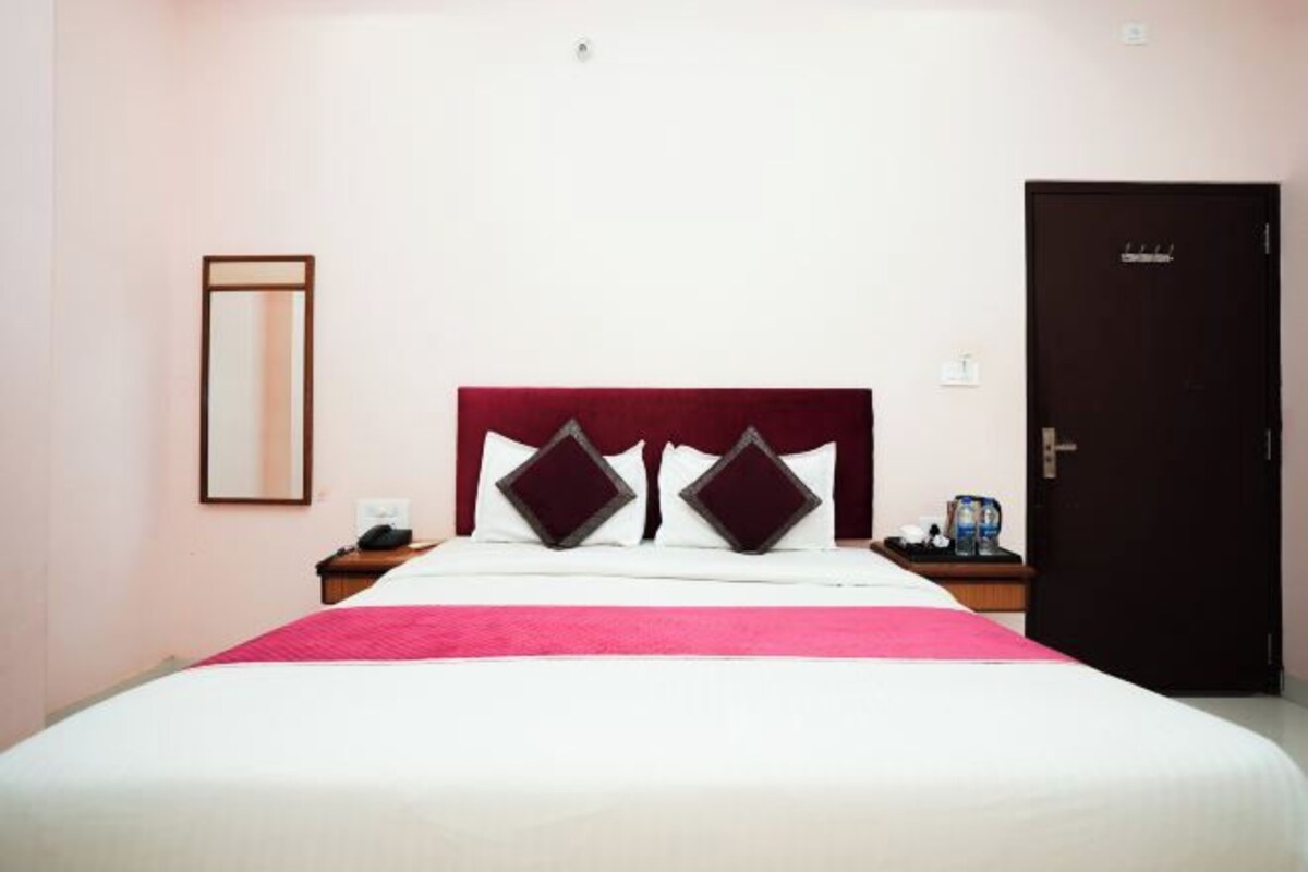 Habitación de hotel con cama, mesita de noche, espejo y puerta.