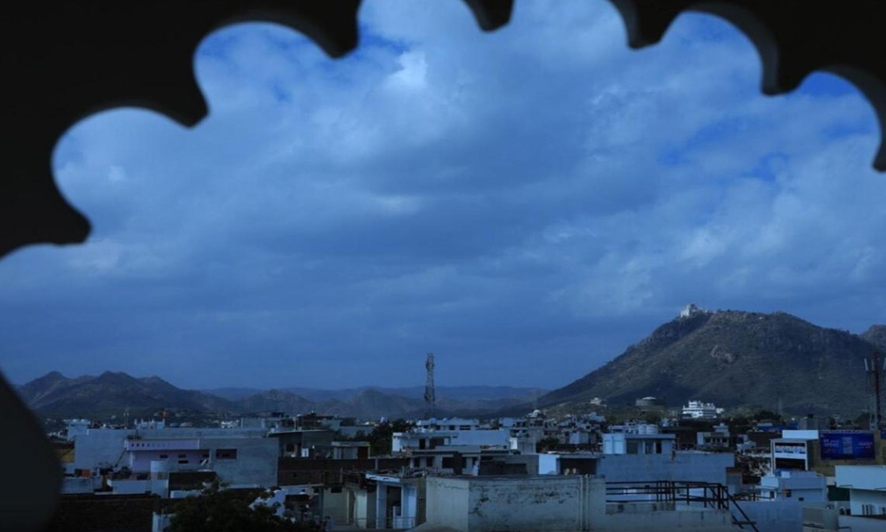 A cityscape with a prominent mountain in the background, a clear sky, and a silhouette of a building with a unique architectural feature in the foreground.