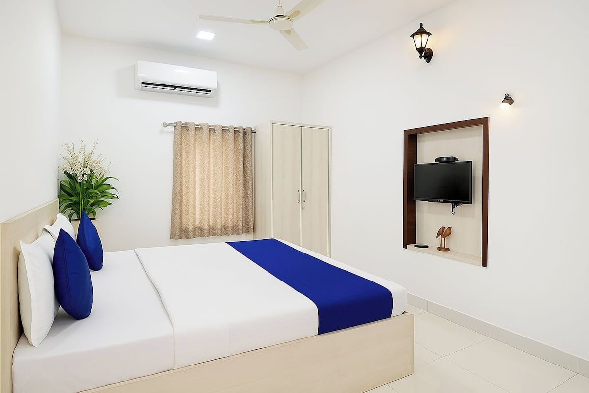 A bedroom with a bed, a ceiling fan, an air conditioner, a TV mounted on the wall, and a plant.