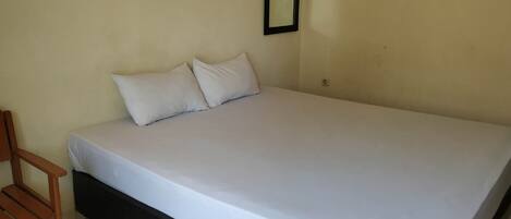A single bed with a white mattress and two pillows, a wooden chair, and a wall-mounted mirror.
