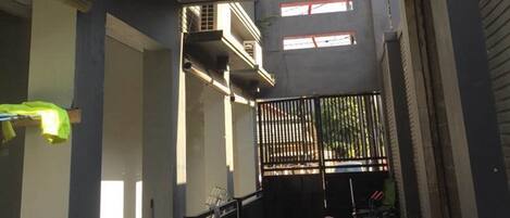 A narrow alleyway with a gated entrance, a motorcycle parked inside, and a building with a grey facade and red accents.