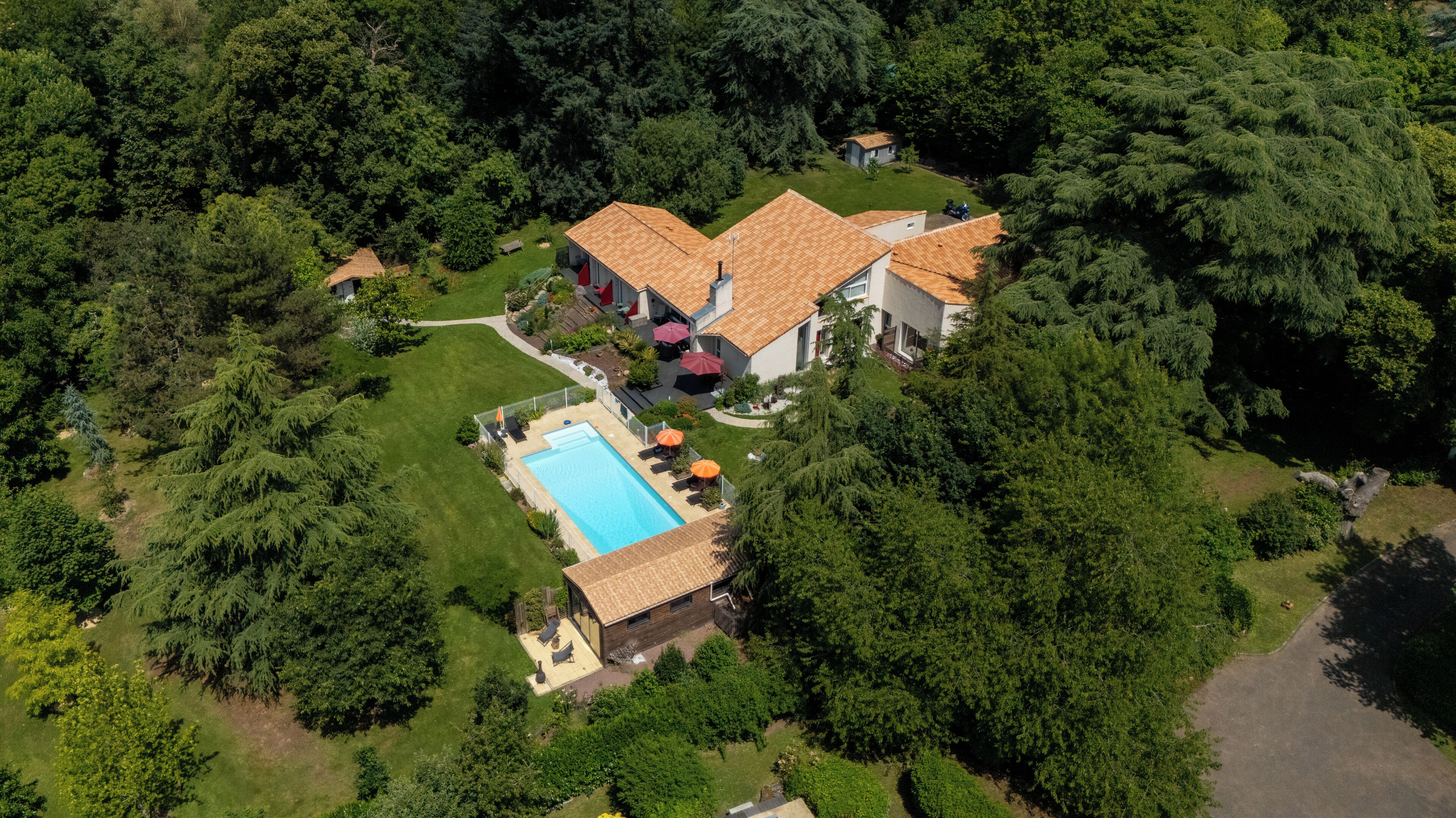 Vue aérienne d’une propriété résidentielle dotée d’une piscine, de plusieurs maisons et d’une végétation luxuriante environnante.