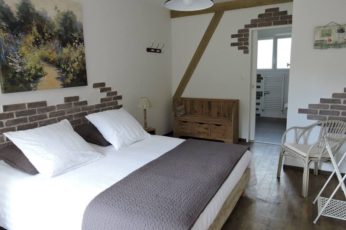 Une chambre à coucher avec un lit, un banc en bois, une chaise et un tableau accroché au mur.