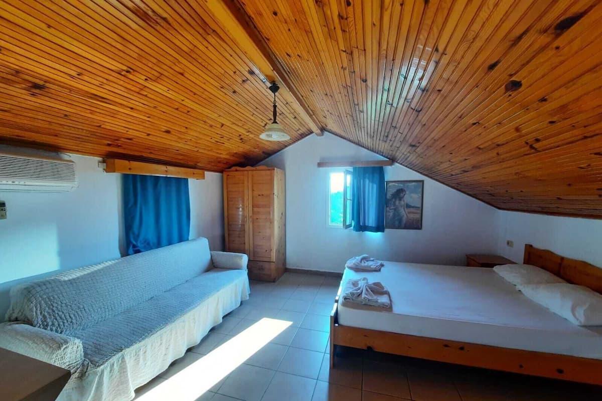 A cozy attic bedroom with a wooden ceiling, a bunk bed, a sofa, and a wardrobe.