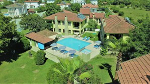A residential area with a large swimming pool surrounded by lounge chairs and umbrellas, a stone staircase, and a view of neighboring houses. - Dalyan Summer Life Apart Hotel (Ortaca)
