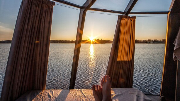 Une personne allongée sur un lit, avec vue sur un coucher de soleil sur l’eau.