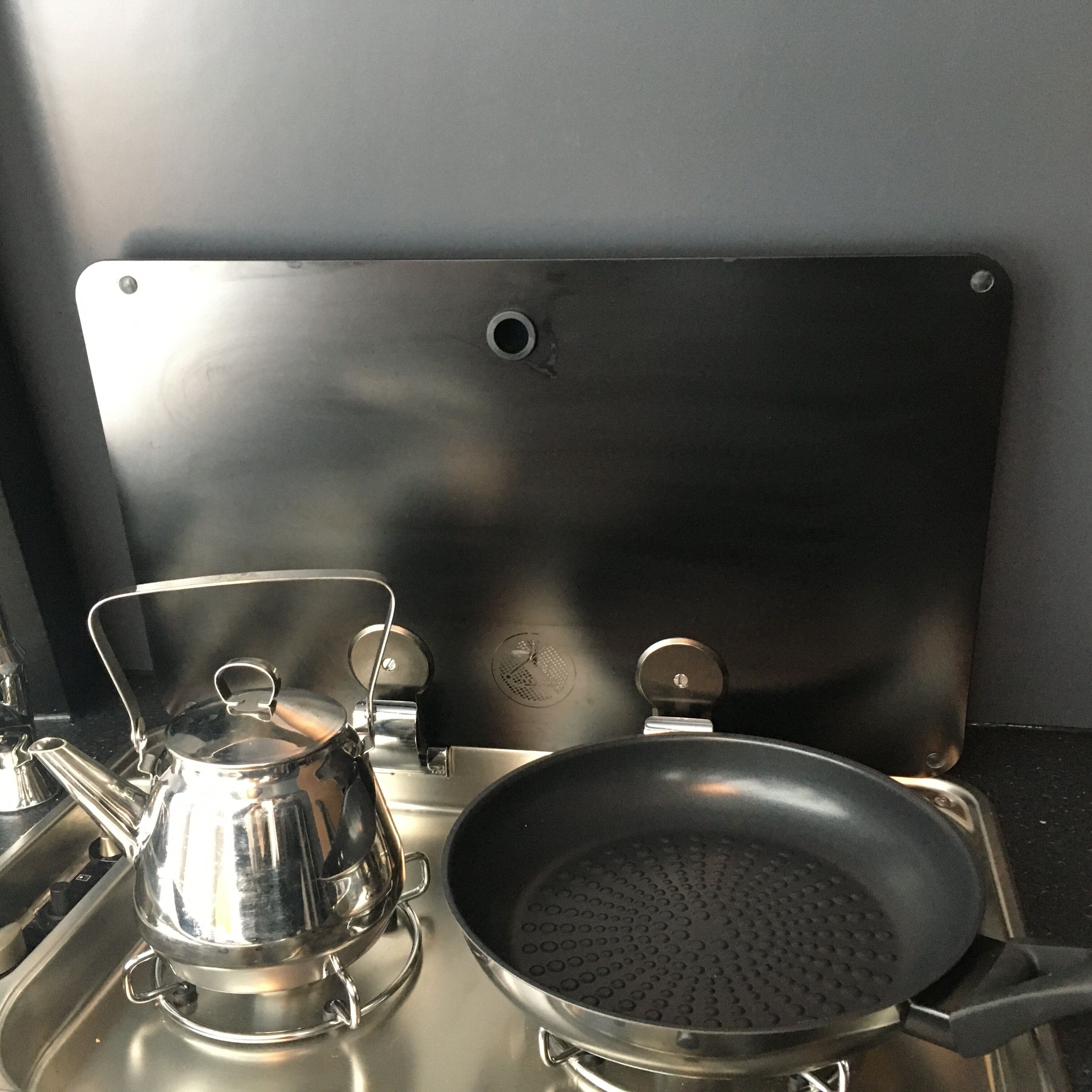 Een keuken met een waterkoker, een koekenpan en een pan op het fornuis.