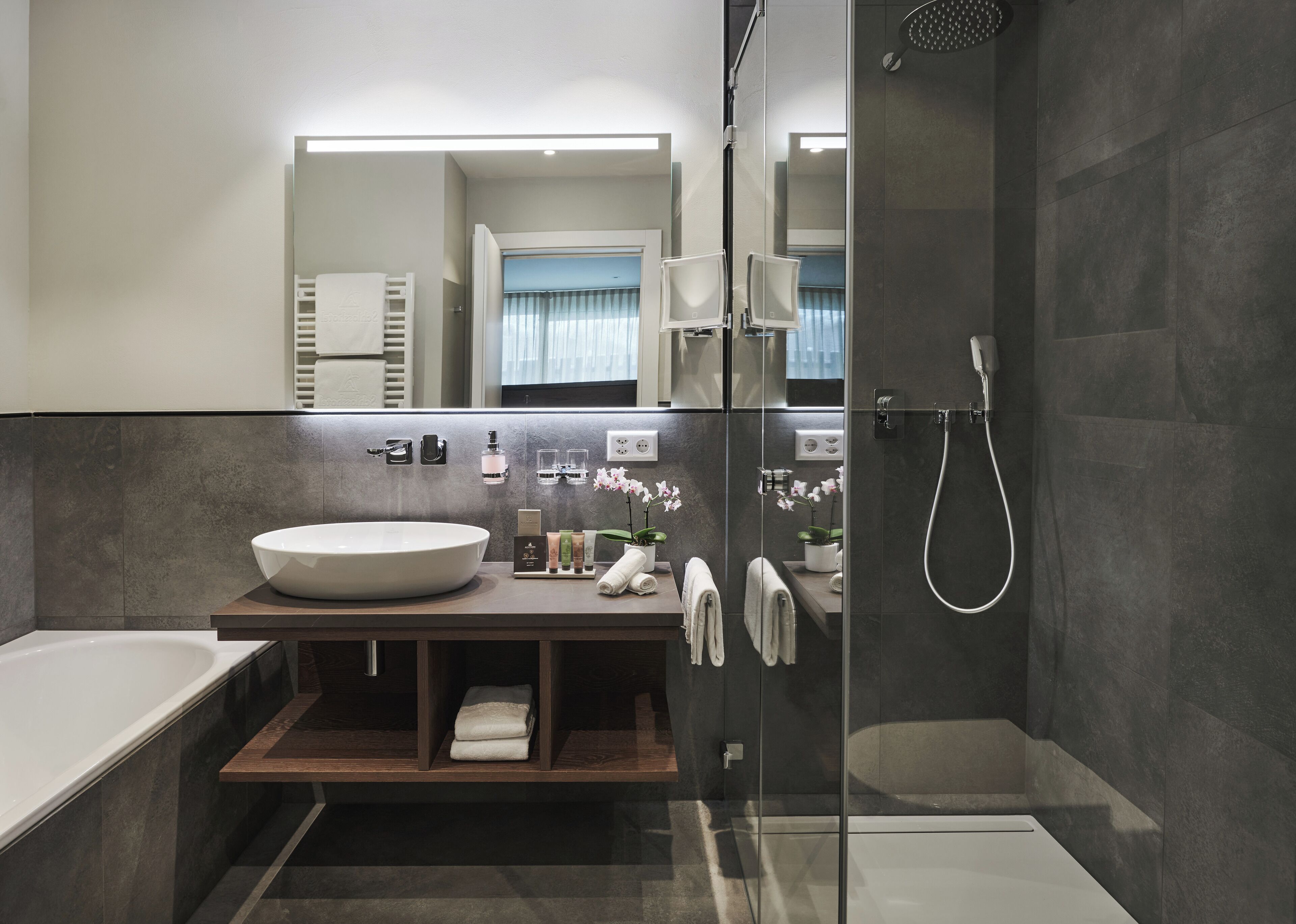 A modern bathroom with a large white sink, a glass-enclosed shower, and a wooden vanity.