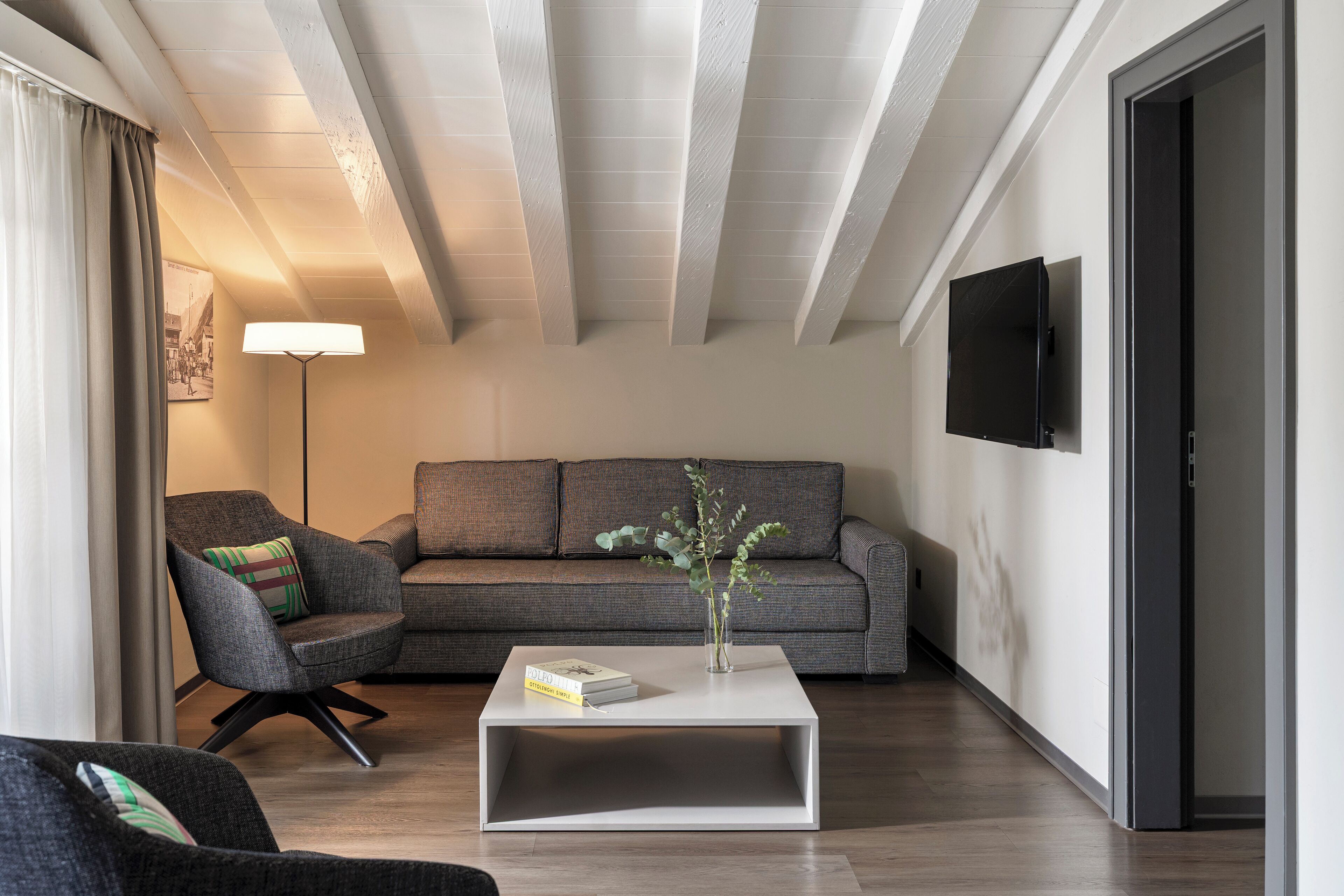 A modern living room with a grey sofa, a white coffee table, and a black TV mounted on the wall.