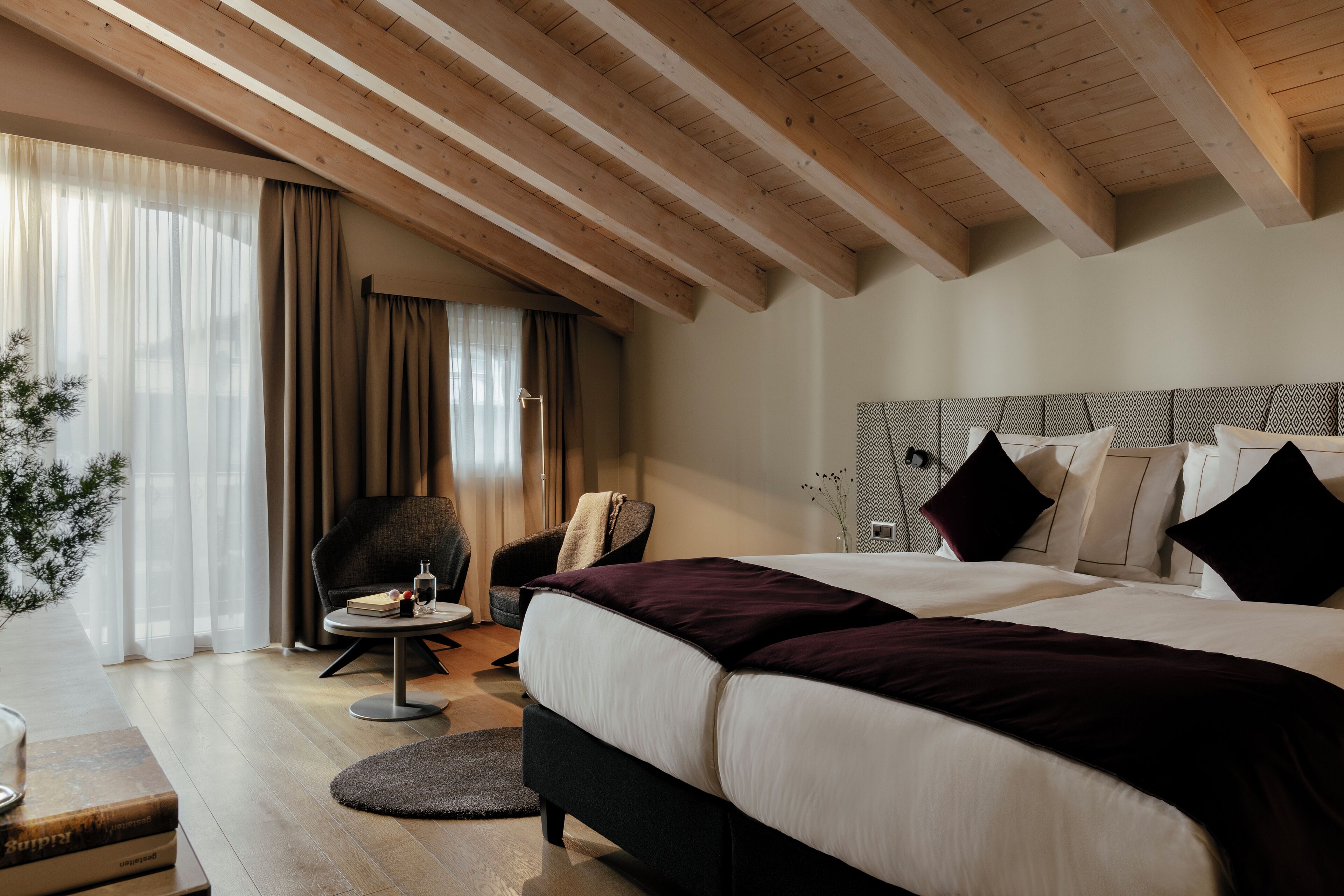 A modern bedroom with a large bed, a desk with a chair, and a window with curtains.