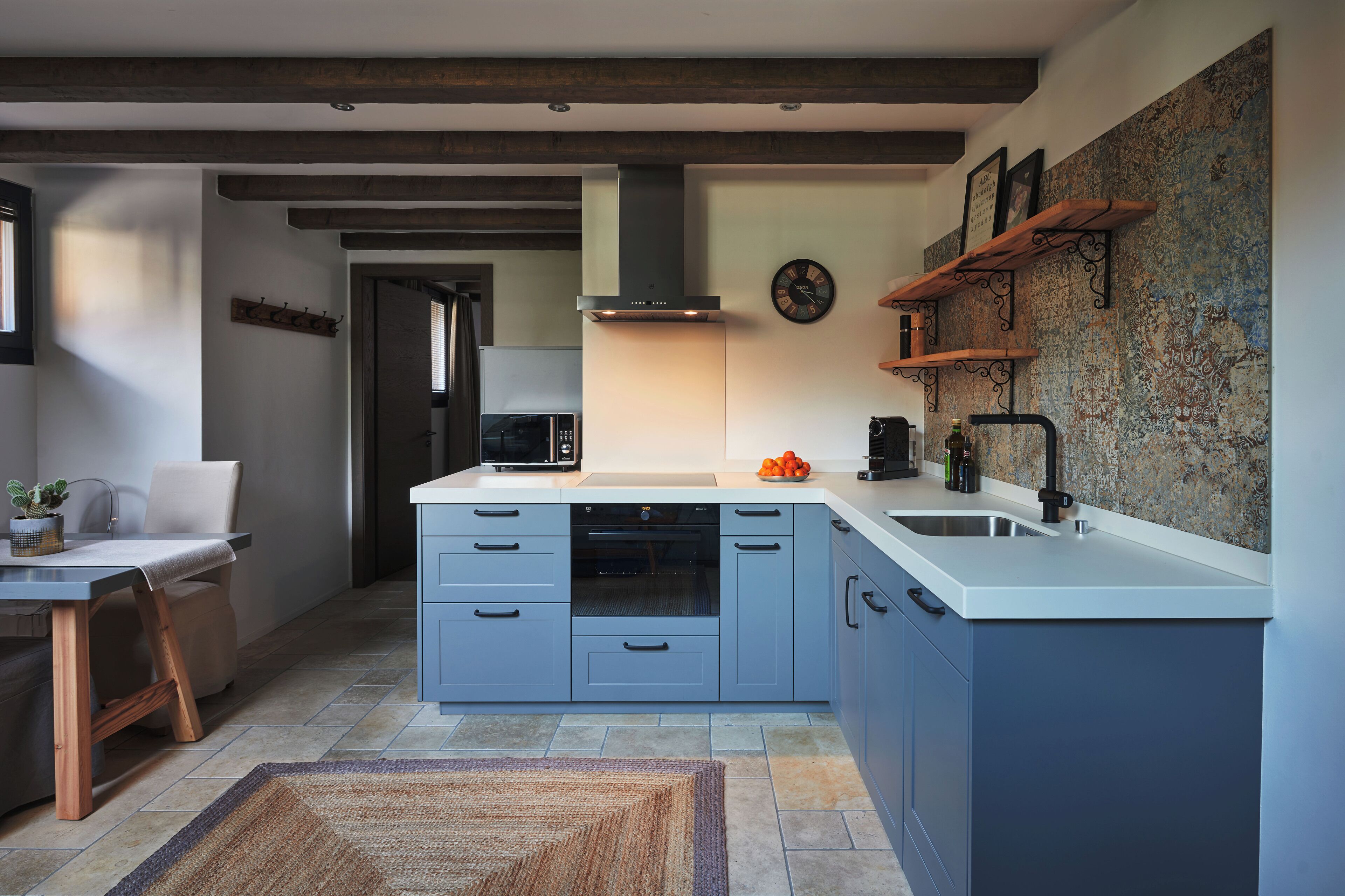 A modern kitchen with blue cabinets, a central island, a built-in oven, and a rustic wall.
