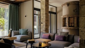 A modern living room with a grey sofa, a small round table, and a stone fireplace. - SCHLOSS Zermatt - CBD & Adaptogenic Spa and Sport Hotel (Zermatt)