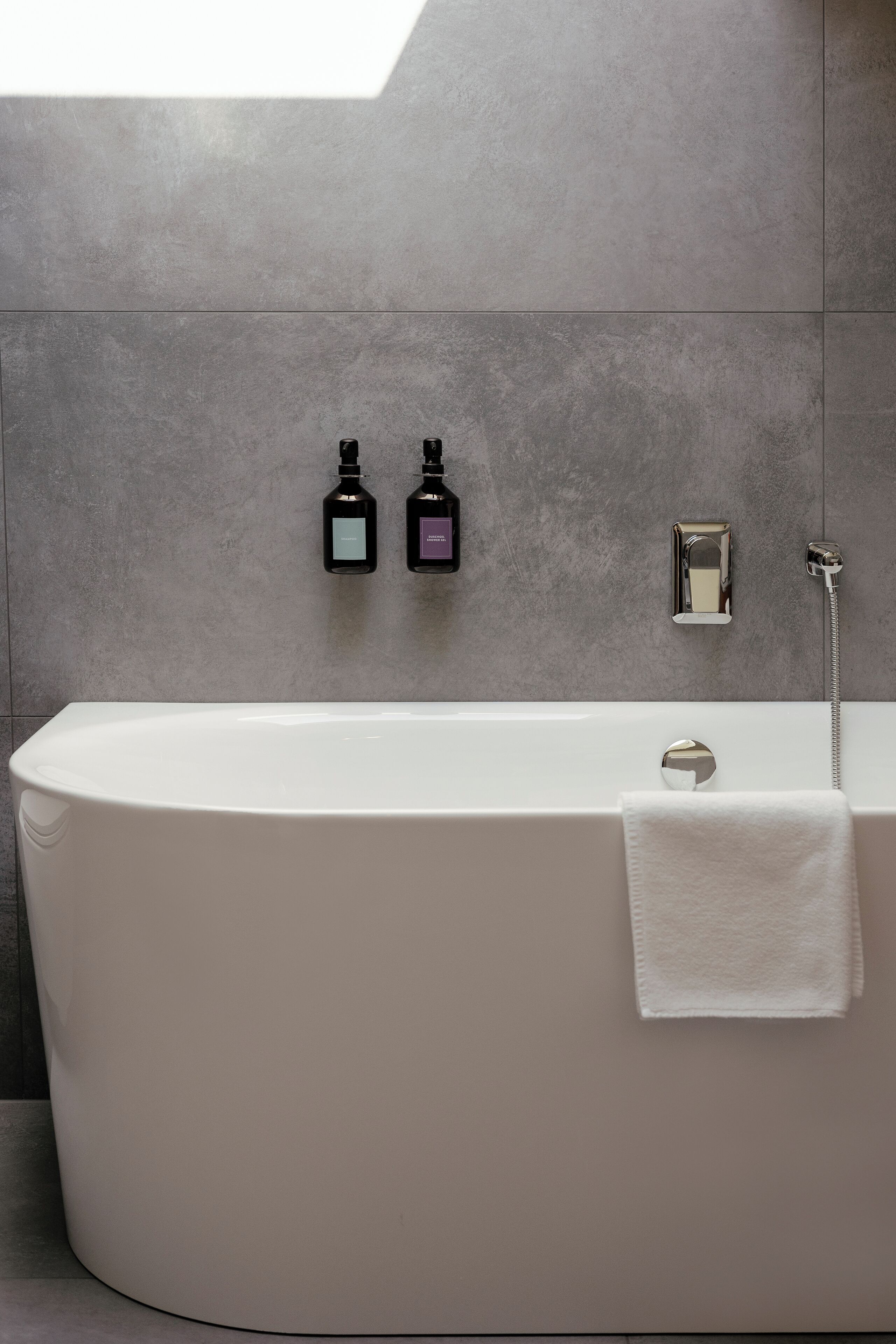 A modern bathroom with a freestanding bathtub, a towel rack, and two bottles of soap on the wall.
