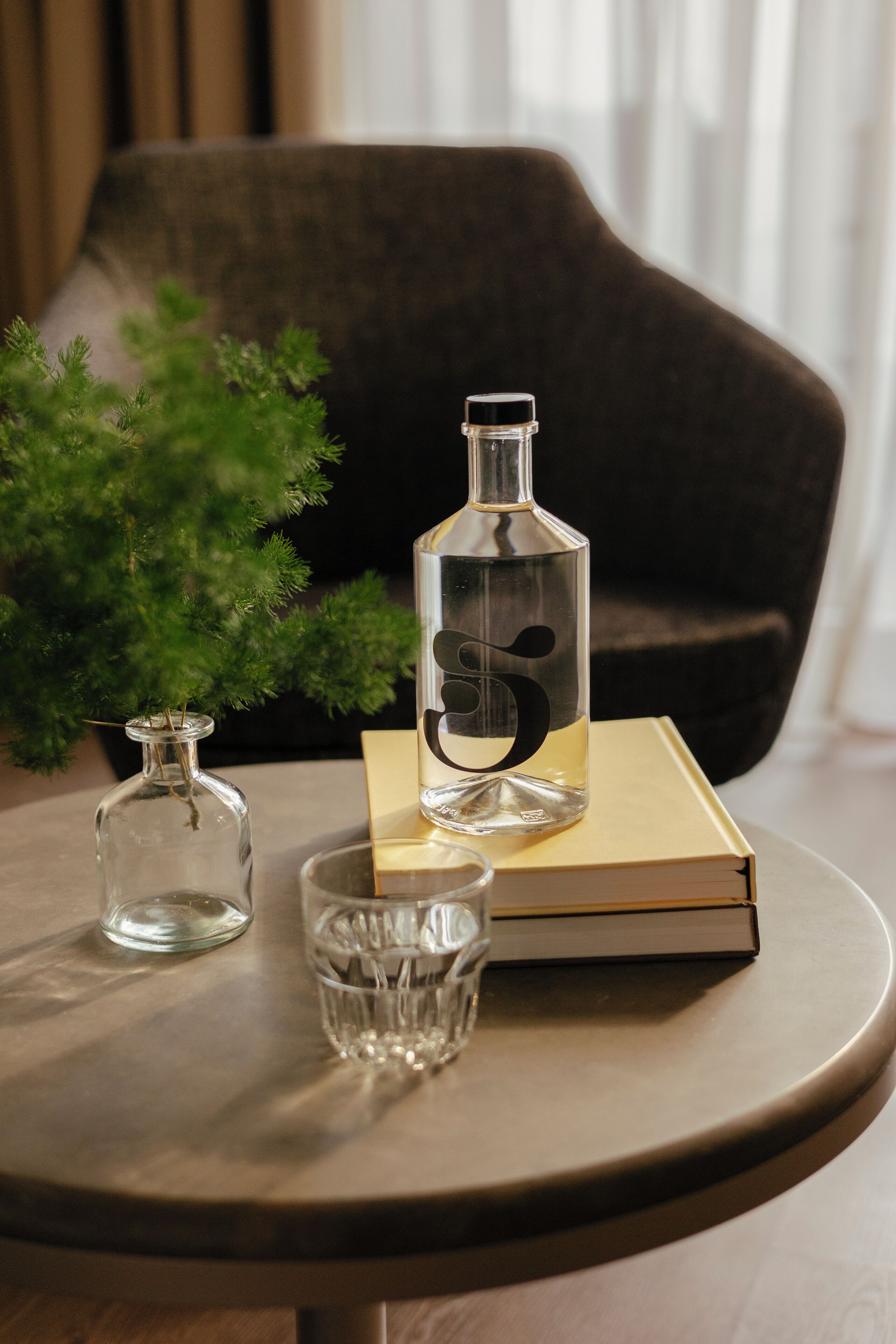 Une table ronde avec une bouteille transparente, un verre et un livre.