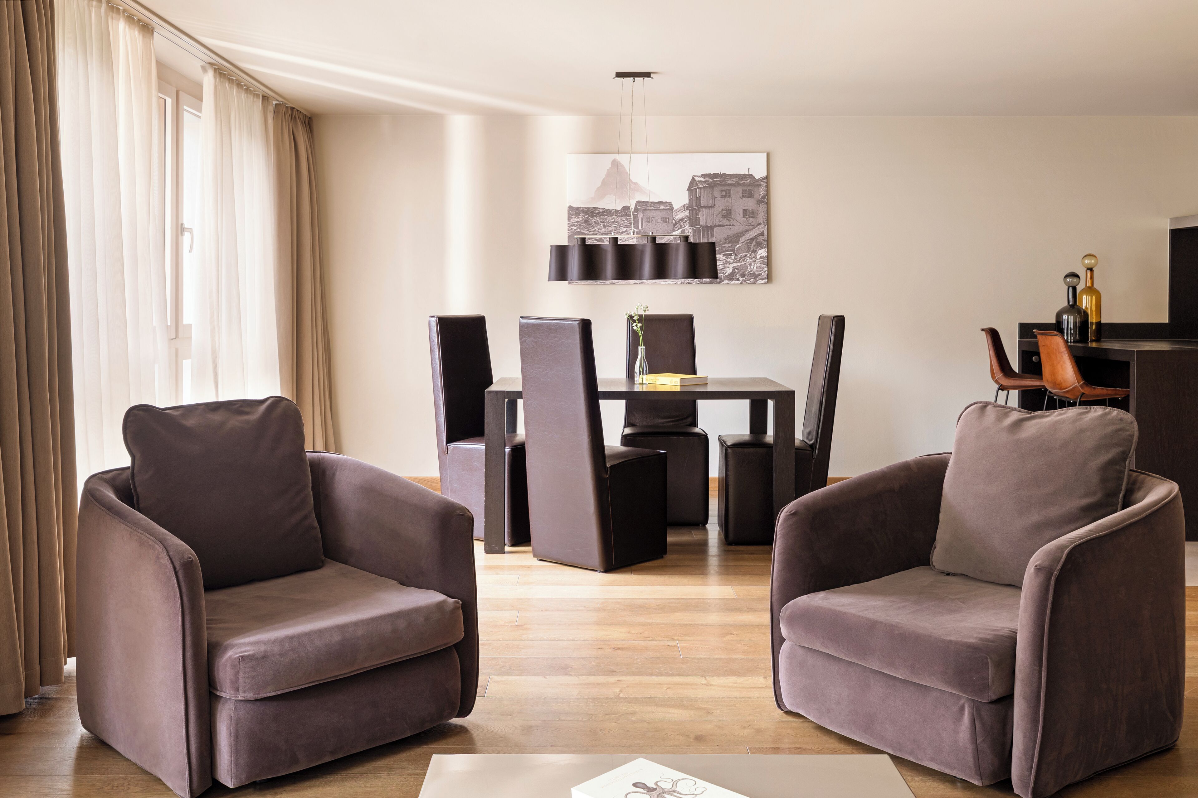Uma sala de estar moderna com dois poltronas, uma mesa de jantar com cadeiras, uma TV de tela plana e um quadro na parede.
