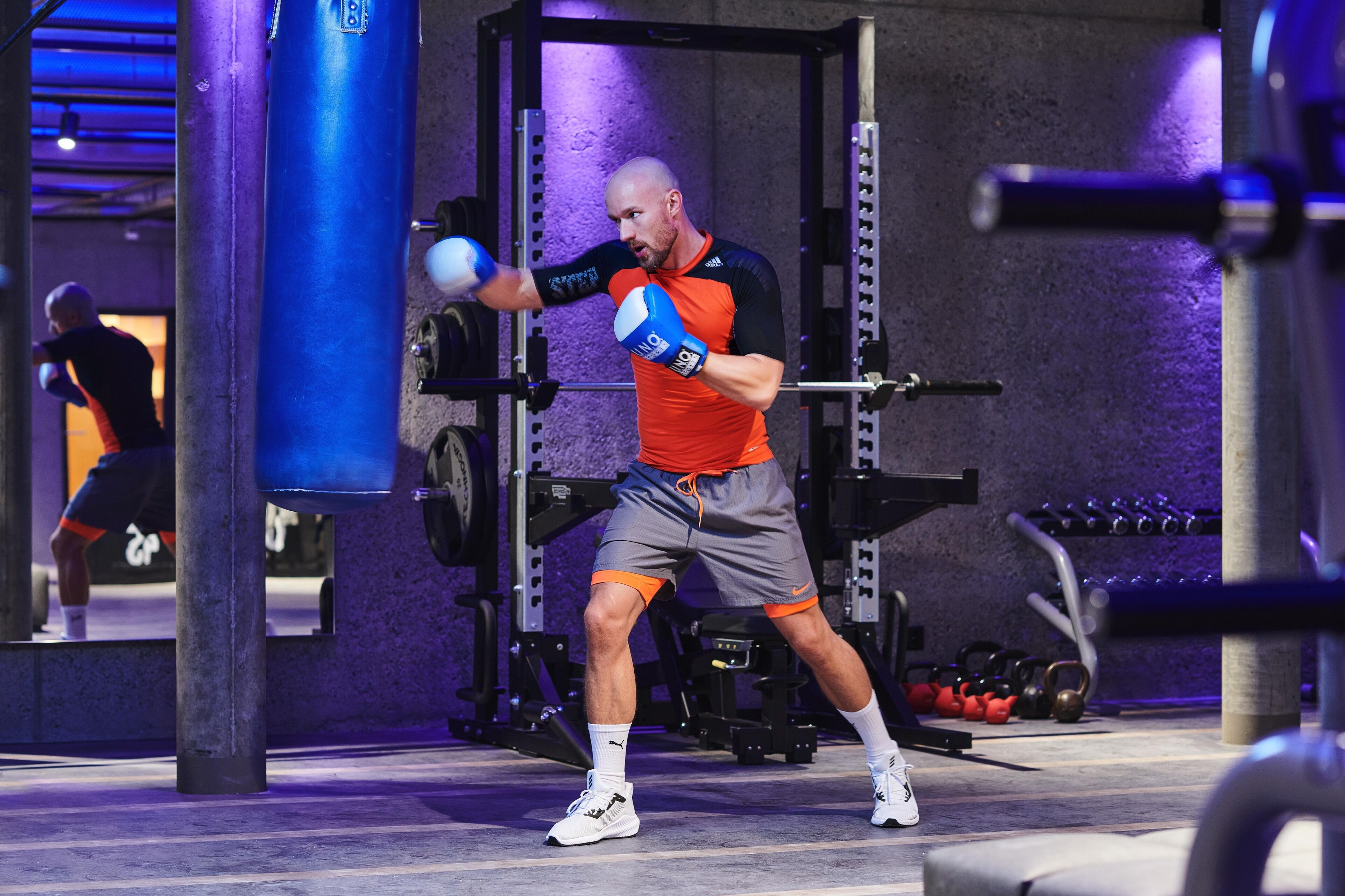 A man in a gym with weightlifting equipment and a punching bag.