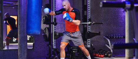 A man in a gym with weightlifting equipment and a punching bag.