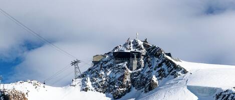 A snow-covered mountain with a building on top, surrounded by rocky terrain and a clear sky.