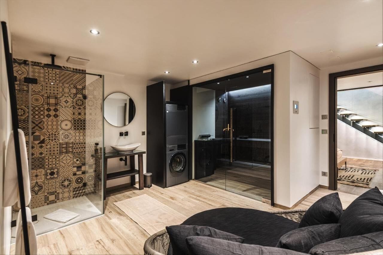 Un baño moderno con pared de baldosas estampadas, espejo redondo, lavabo y cabina de ducha con mampara de vidrio.