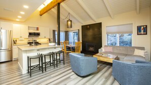 A modern kitchen with a central island, dining area with chairs, a sofa, and a fireplace. - Experience the best of Ketchum-living in a newly remodeled mountain modern condo (Ketchum)