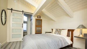 A bedroom with a bed, a nightstand, a lamp, a sliding door, and a ceiling with exposed beams. - Experience the best of Ketchum-living in a newly remodeled mountain modern condo (Ketchum)