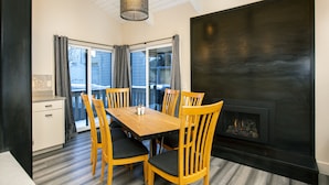 A dining area with a wooden table and chairs, a fireplace, and a view through large windows. - Experience the best of Ketchum-living in a newly remodeled mountain modern condo (Ketchum)