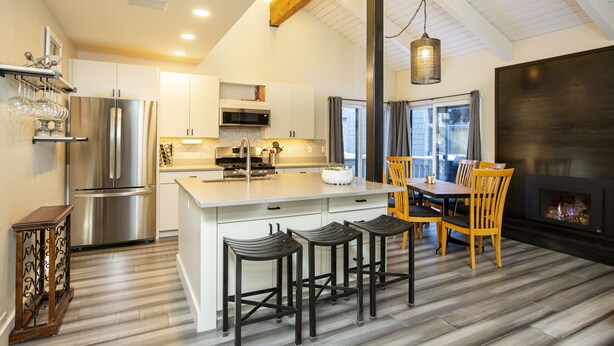 A modern kitchen with a central island, stainless steel appliances, and a dining area with wooden chairs and a table. - Experience the best of Ketchum-living in a newly remodeled mountain modern condo (Ketchum)
