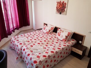 A neatly made bed with floral bedding, a bedside table, and a wall-mounted painting. - Vintegra Family Hotel (Burgas)