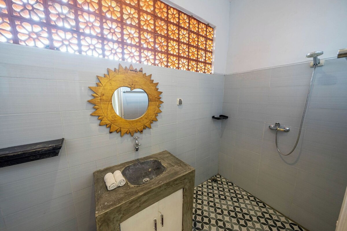 A bathroom with a sunburst mirror, a sink with a towel, a shower, and patterned floor tiles.