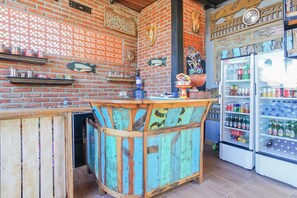 A bar area with a wooden counter, shelves with drinks, and a refrigerator stocked with beverages. - Art Canggu Village (Canggu)