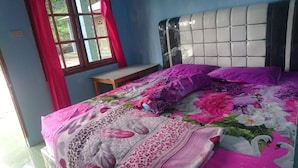 A bed with a floral bedspread and two pillows, a wooden nightstand, and a window with red curtains.