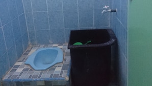 A small bathroom with a blue toilet, a black trash bin, and a green cleaning brush.