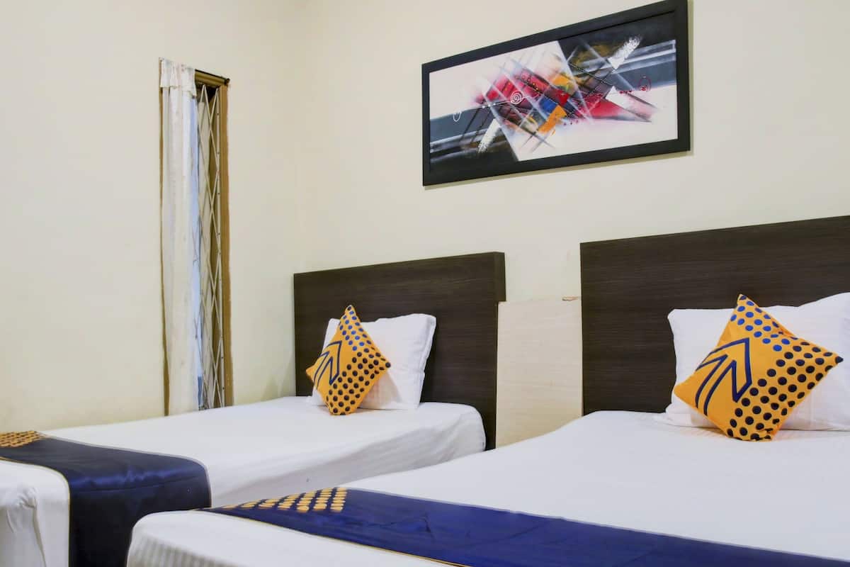 A hotel room with two single beds, each with a white pillow and a patterned pillow. There is a framed abstract painting on the wall above the beds.