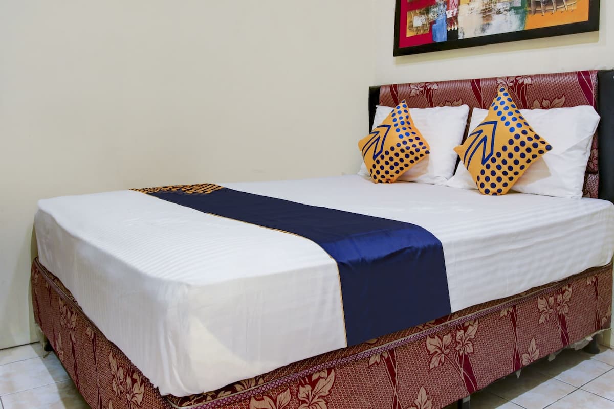A neatly made bed with white and navy blue bedding, two decorative pillows with yellow and blue patterns, and a red patterned bed skirt.