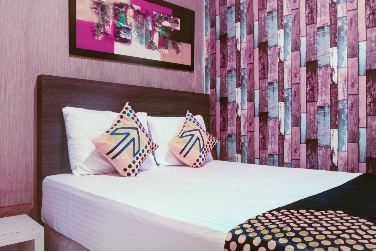 A neatly made bed with two pillows, a framed artwork above it, and a wooden wall panel.