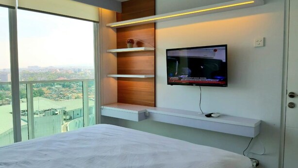 Una habitación de hotel moderna con una cama grande, un televisor montado en la pared y un balcón con vistas a la ciudad.