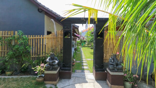 A garden pathway leading to a building with a wooden fence and statues. - Kompyang Rai Guest House (Canggu)