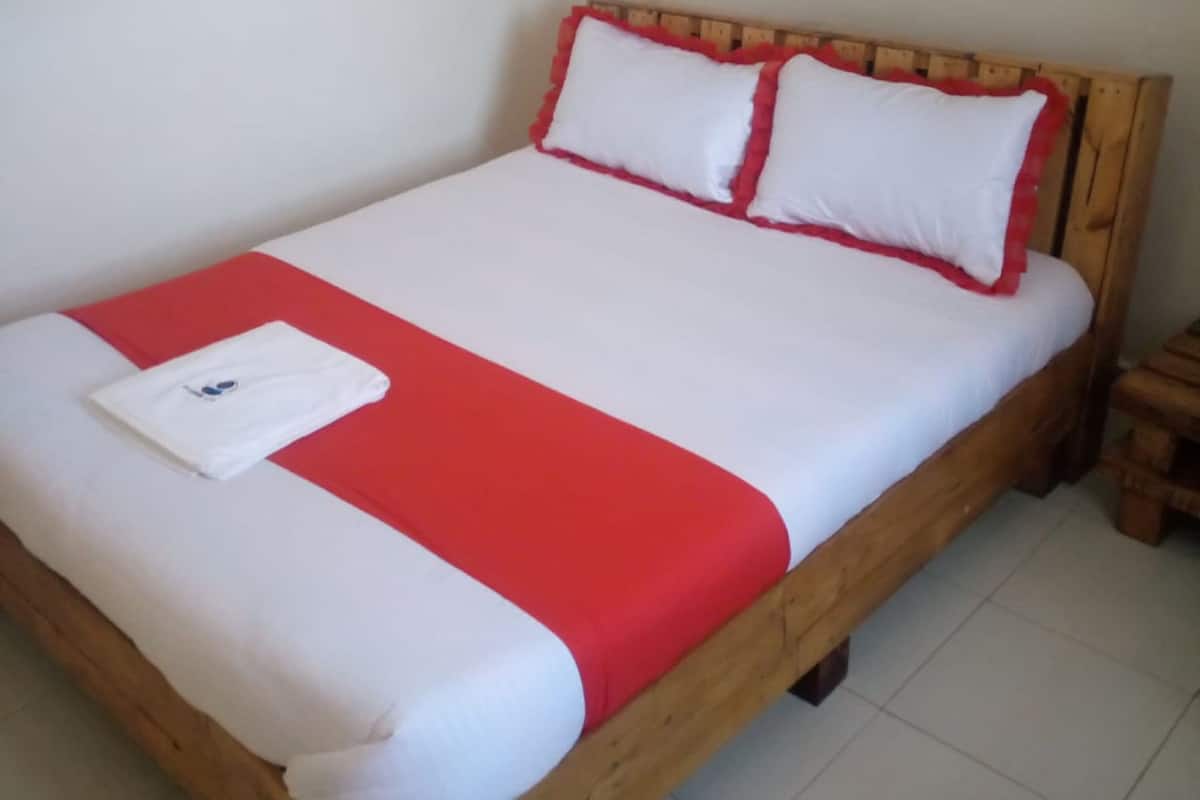 Een houten bed met wit en rood beddengoed, een witte handdoek op het bed en een houten nachtkastje ernaast.