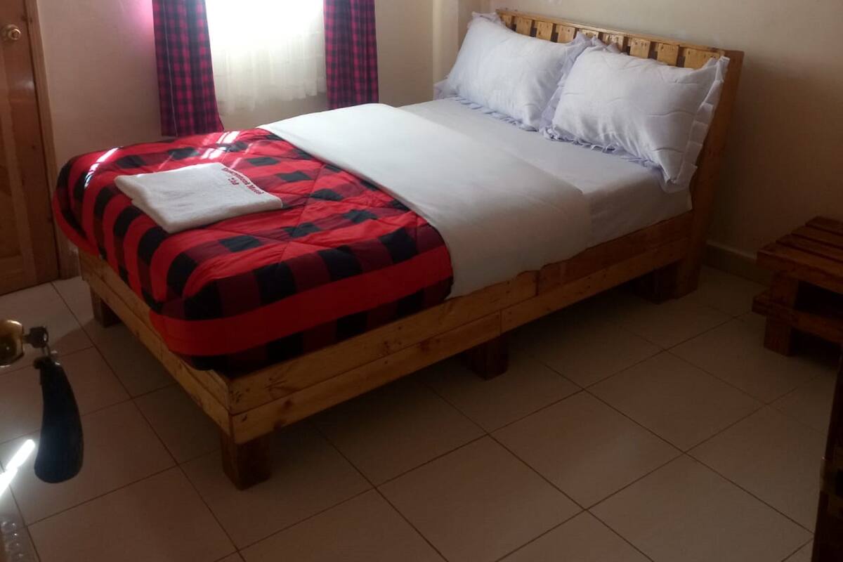 Een houten bed met een rood-zwart geruit sprei, witte kussens en een witte deken.