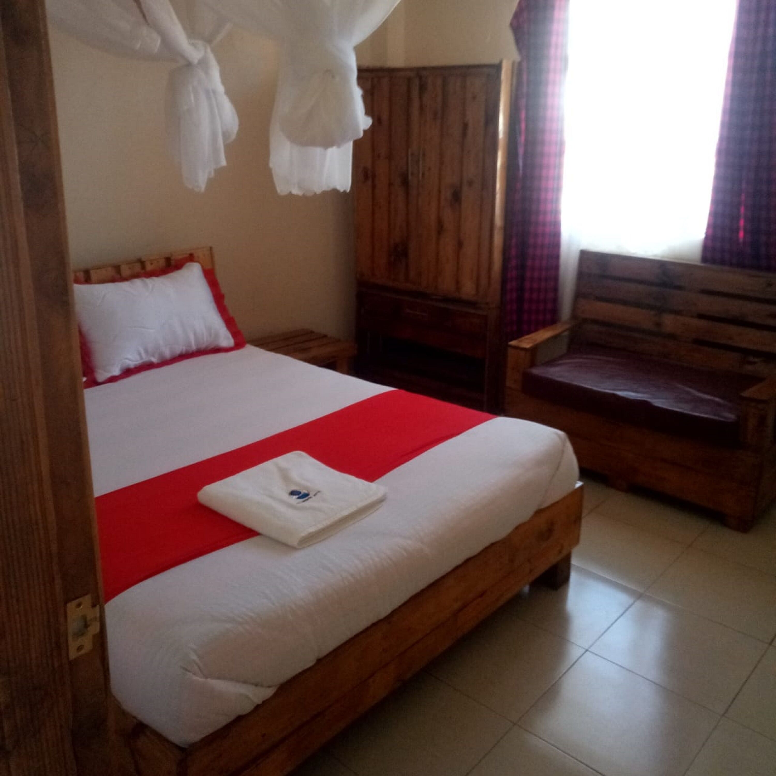 A wooden bed with a red blanket, a wooden nightstand, a wooden wardrobe, and a wooden chair.