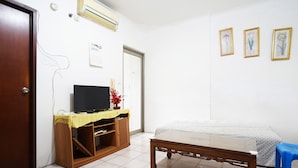 Een kamer met een bed, een houten tafel, een televisie op een standaard en een wandairconditioner.