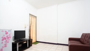 Een woonkamer met een flatscreen televisie op een zwarte standaard, een bruine bank en een witte koelkast met roze bloemen.