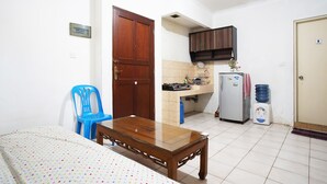 Een kleine, schone kamer met een bed, een houten tafel, een blauwe stoel, een kitchenette en een waterdispenser.