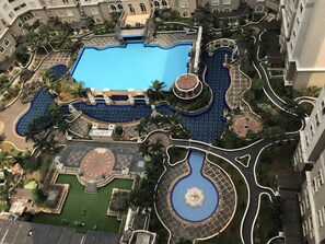 Une grande piscine entourée de jardins aménagés, une fontaine centrale et une place circulaire au décor ornemental.