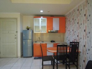 Eine kleine Küche mit Kühlschrank, Spüle und orangefarbenen Schränken. Ein Esstisch mit Stühlen steht bereit.
