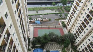 A high-rise building with multiple balconies, a central courtyard with a swimming pool, and a tennis court.