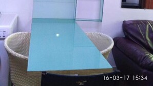 A room with a glass-top table, dark cabinets, a wicker chair, and a purple sofa.